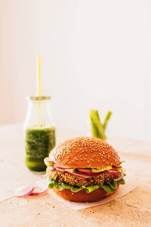 Vegetarian burger with a bottle of green smoothie and carrot with celery in a glass. Stone beige tableの写真素材