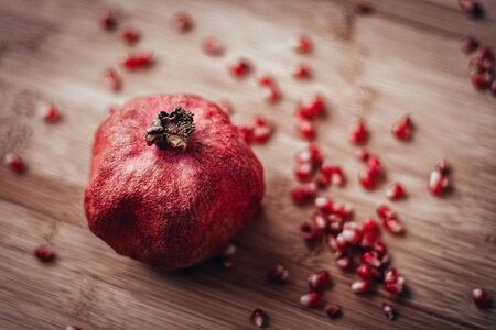 red pomegranate with sprinkled grains on a wooden background
