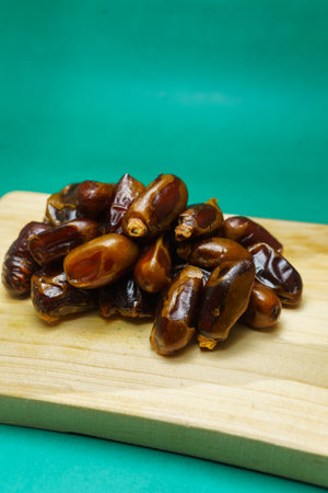 Dates fruit on a wooden cutting board on a green background.