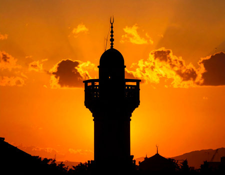 Dramatic mosque minaret stands silhouetted against a vibrant orange sunset sky evoking a sense of peace and spirituality Ideal for religious or travel themes.の素材
