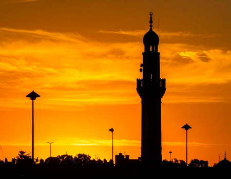 Dramatic mosque minaret stands silhouetted against a vibrant golden sunset sky evoking a sense of peace and spirituality Ideal for religious or travel themes.の素材