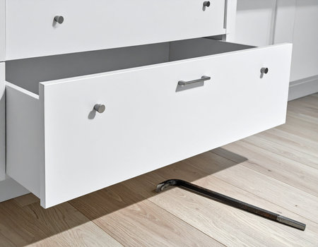 A white dresser drawer is partially open revealing its interior with a black wrench lying on the wooden floor Use for home repair or security concepts.の素材