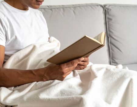 Relaxed man enjoys reading a book while resting comfortably under a soft blanket Perfect for illustrating leisure and relaxation.の素材