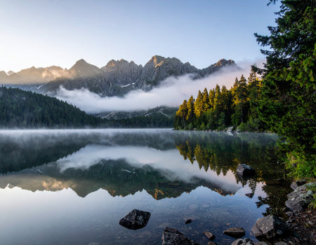 Serene alpine lake mirrors surrounding mountains shrouded in morning mist creating a peaceful atmosphere Ideal for nature and landscape projectsの素材