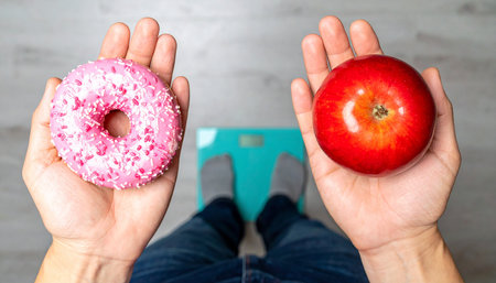 Female hands holding a donut and an apple on the scales.の素材