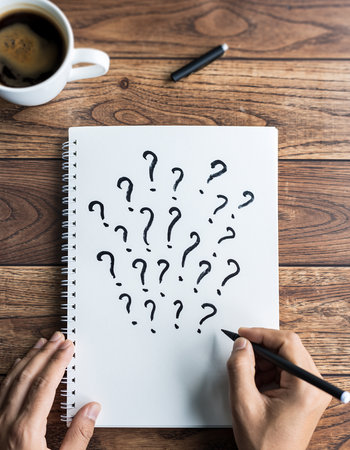 Person writing question marks in a notebook with coffee and pen on wood Clear details and vibrant colors enha...の素材