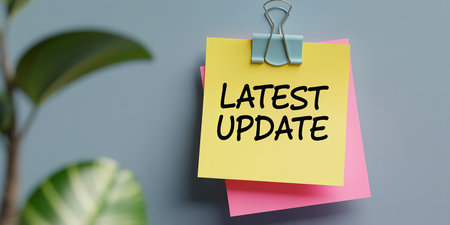 Yellow sticky note with 'Latest Update' text held by a clip on a gray wall with plantの素材