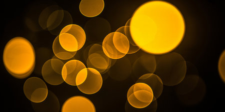 Soft, out of focus yellow circles of light create a warm bokeh effect against a dark backgroundの素材