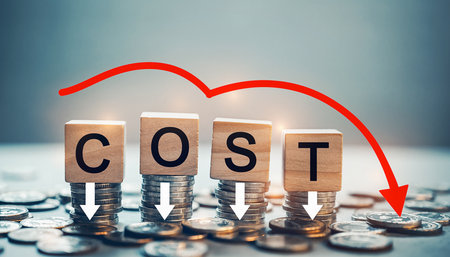 Wooden blocks spelling COST stacked on coins with a red arrow indicating a sharp downward trend.の素材