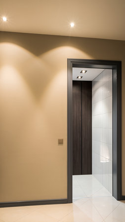 A modern interior hallway with a beige wall and an open doorway revealing a tiled room.の素材