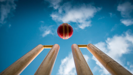 A red cricket ball flies in the air above wooden stumps against a blue sky. Clear details and vibrant colors ...の素材