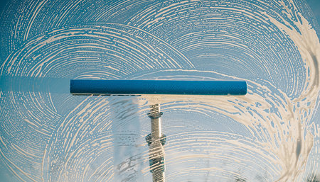 A blue squeegee tool with foam creates swirling patterns while cleaning a window.の素材