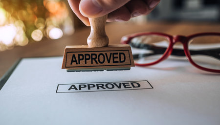 Hand stamping the word APPROVED on a piece of paper with red glasses in the backgroundの素材