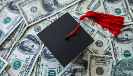 A black graduation cap with a red tassel rests on a pile of US dollar bills. Clear details and vibrant colors...の素材