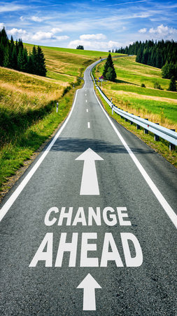 Open road with CHANGE AHEAD painted on asphalt leading through green rolling hillsの素材