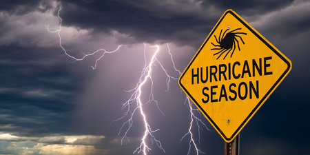 A yellow diamond warning sign reads HURRICANE SEASON against a dramatic stormy sky with lightning.の素材