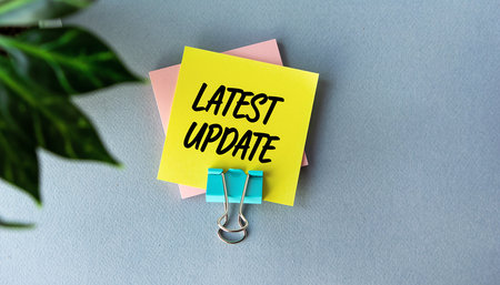 Yellow sticky note with 'LATEST UPDATE' text and binder clip on gray Clear details and vibrant colors enhance...の素材
