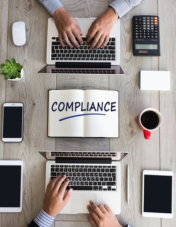 Business meeting with laptops, tablets, and a notebook displaying the word COMPLIANCEの素材