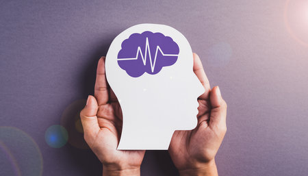 Hands cradle a white paper head cutout with a purple brain and heartbeat line. Clear details and vibrant colo...の素材