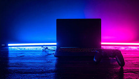 Laptop computer on table in dark toned foggy room with neon light. Selective focusの素材