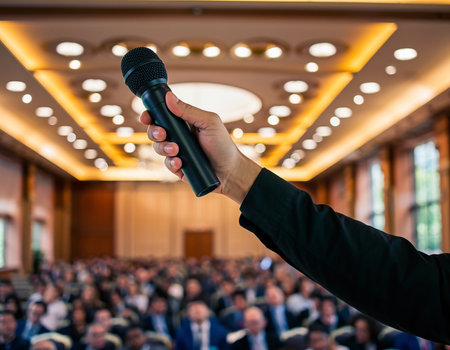 Businessman holding a microphone in front of a crowd in conference hallの素材