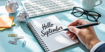 Hand writing hello september in notepad with keyboard and office suppliesの素材