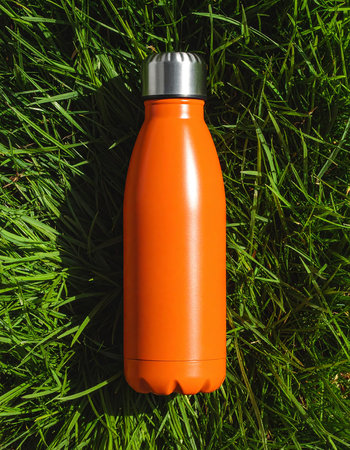 Orange plastic water bottle on green grass background. Flat lay, top viewの素材