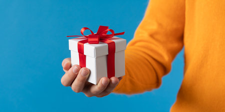 Man holding a gift box with a red ribbon on a blue backgroundの素材