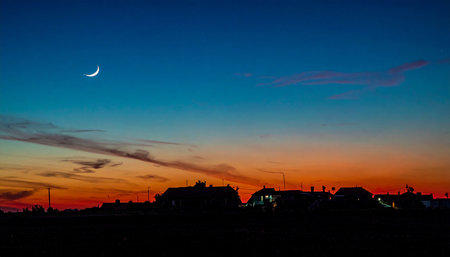 Sunset with a crescent moon in the sky over the villageの素材