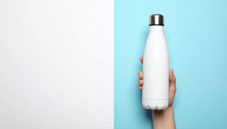 Female hand holding thermos bottle on blue and white background, top viewの素材