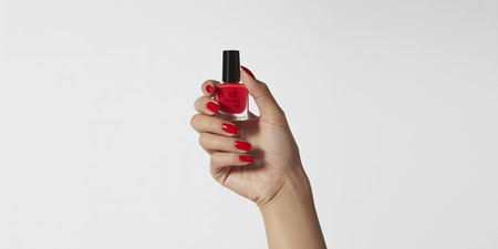 Woman hand with red manicure holding nail polish isolated on white backgroundの素材