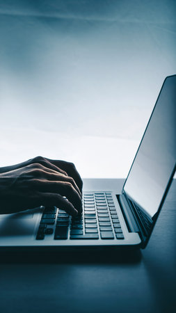 Close-up of female hands typing on laptop keyboard on dark backgroundの素材