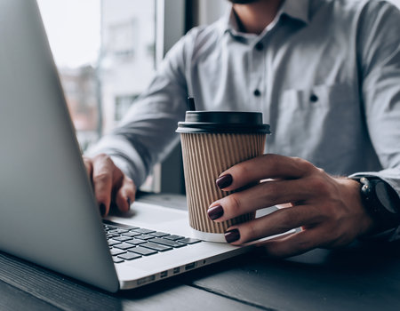 Cropped image of young businessman holding coffee cup and using laptop in cafeの素材