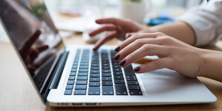 Close-up of female hands typing on laptop keyboard at office deskの素材