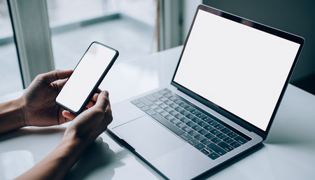 Mockup image of hands using laptop and mobile phone with blank white screenの素材