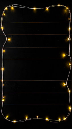 Christmas lights on black wooden background. Top view with copy space.の素材