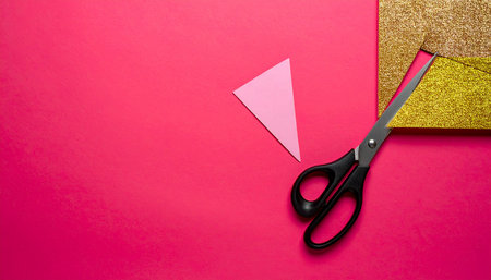 Scissors cutting a red paper on a pink background with copy spaceの素材