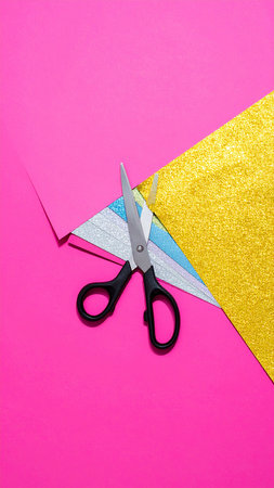Scissors cutting colored paper on pink and yellow background. Top viewの素材