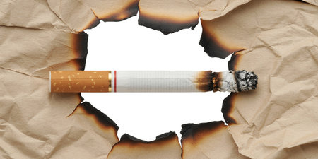 Cigarette breaking through a hole in paper, isolated on whiteの素材