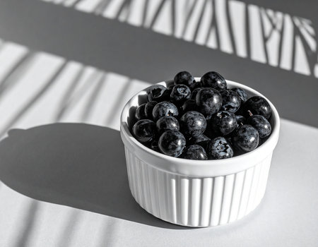 Fresh blueberries in a white bowl on a light background with shadows.の素材