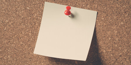 Blank note paper pinned to cork board with red pin.の素材