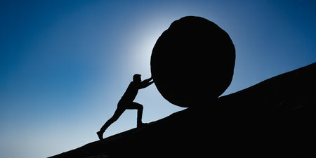 Silhouette of a man pushing a huge ball on a wallの素材