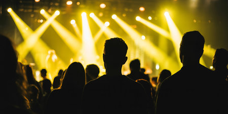 Silhouette of a concert crowd in front of a bright stage lightsの素材