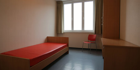 Interior of a hotel room with red bed and a small windowの素材