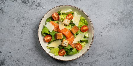 Salad with salmon, cheese and vegetables in bowl on stone background. Top viewの素材