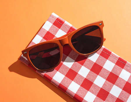 Sunglasses with red checkered towel on orange background.の素材