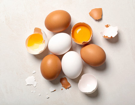 Broken eggshell and raw chicken eggs on white table, top viewの素材