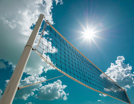 Volleyball net against blue sky with clouds and sun in backgroundの素材