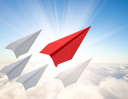 Leadership concept with red paper plane leading among white paper planes in the cloudsの素材