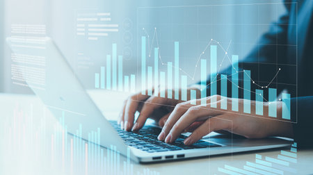 Close up of businesswoman hands typing on laptop keyboard. Financial graph hologram. Double exposureの素材